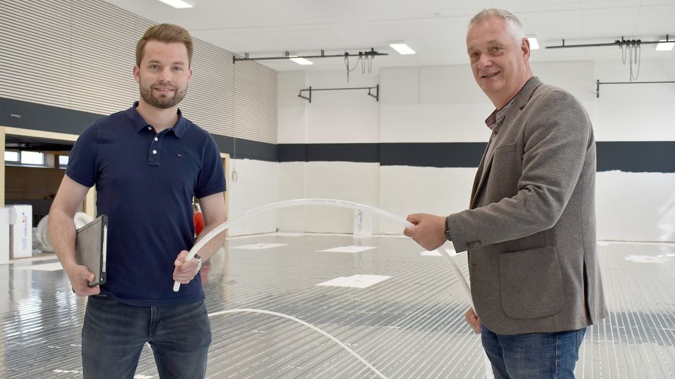 Bürgermeister Günter Harders (rechts) und Bauleiter Sebastian Meyer halten eine der Leitungen hoch, die für die Fußbodenheizung verlegt werden.