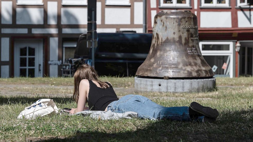Eine Frau liegt vor einer Kirchenglocke an der Göttinger St-Albanikirche in der Sonne. Foto: Swen Pförtner/dpa Foto: Swen Pförtner