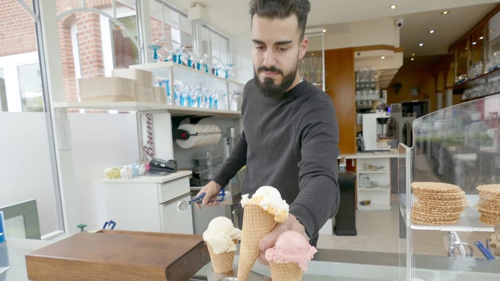 Ali Remmo, stellvertretender Geschäftsführer bei „Bei Bruno“ in Rhauderfehn, überreicht drei Eiswaffeln. Foto: Wieking