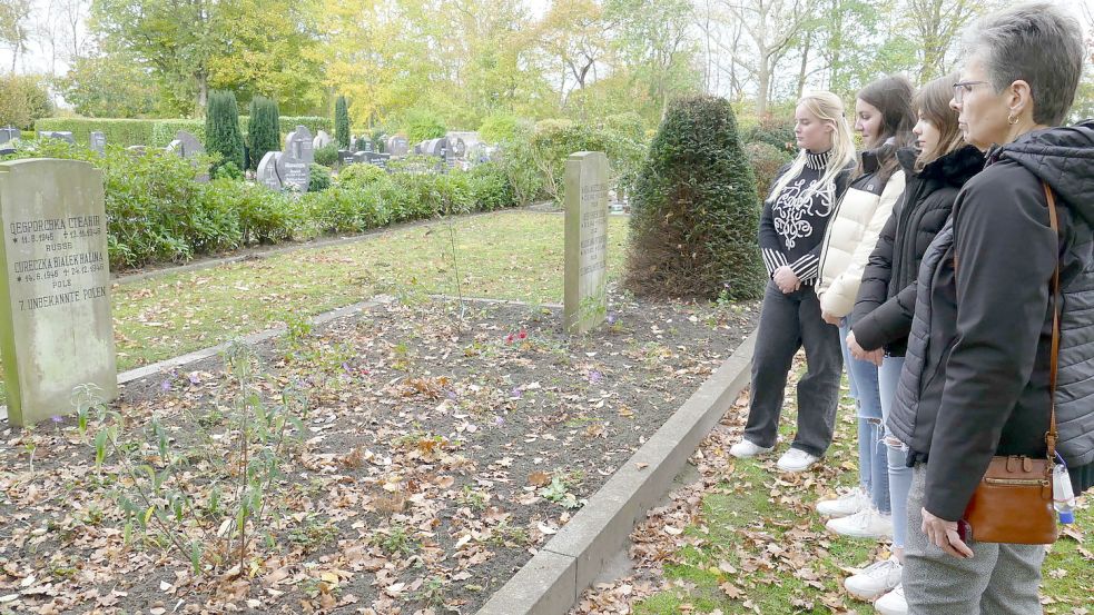 Dr. Halina Woroncow vor dem Massengrab mit Kindern von Zwangsarbeiterinnen aus Polen, der Ukraine und Russland auf dem katholischen Friedhof in Langholt. Dort liegt auch ihr Bruder Viktor, der im Februar 1946 als Baby an einer Lungenentzündung gestorben war. Mit dabei: (von links) Indy Backx, Maila Buskohl und Fenna Seemann, die an der Schule am Osterfehn im vergangenen Jahr den Wahlpflichtkurs Geschichte der Klasse R8a besucht haben. Foto: Wieking