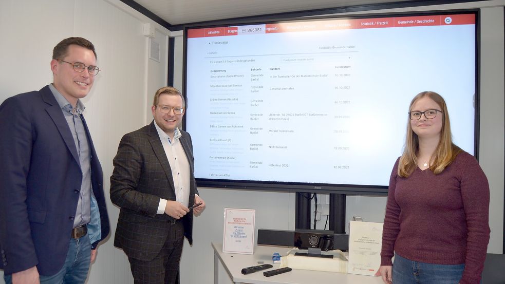 Auf der großen Leinwand im Bürocontainer vor dem Rathaus präsentieren hier (von links) Barßels Ordnungsamtsleiter Dennis Lüthje, Bürgermeister Nils Anhuth und Verwaltungsmitarbeiterin Vanessa zu Klampen den Online-Auftritt des Barßeler Fundbüros. Foto: Fertig