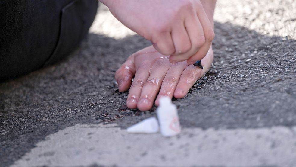 Ein Klimaaktivist klebt seine Hand auf einer Fahrbahn fest. Foto: Lennart Preiss/dpa