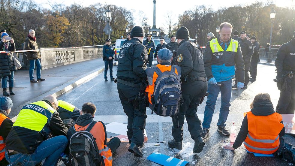 Polizisten tragen in München einen Klimaaktivisten der „Letzten Generation“ weg, der sich zuvor auf der Prinzregentenstraße auf den Asphalt geklebt hatte. Foto: Lennart Preiss/dpa