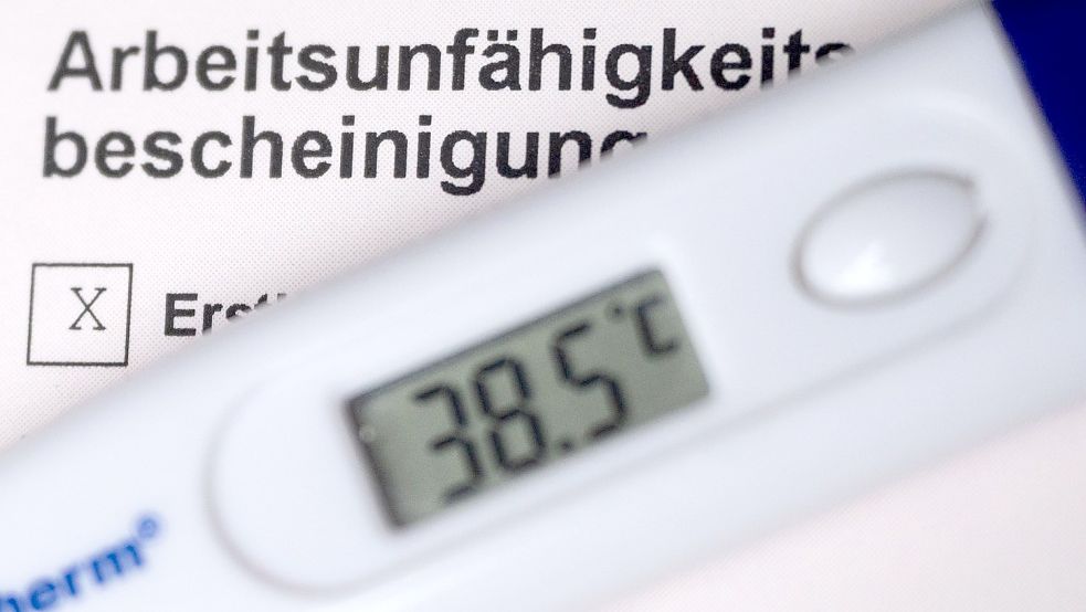 Ein Fieberthermometer liegt auf einer Arbeitsunfähigkeitsbescheinigung. Zum ersten April ist die telefonische Krankschreibung ausgelaufen. Das kritisieren Ostfrieslands Kassenärzte. Foto: Murat/dpa