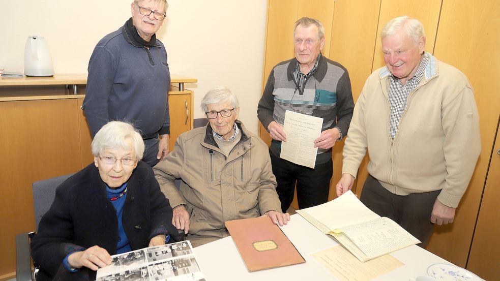In alten Fotos und Schulunterlagen blättert die ehemalige Lehrerin Ruth Pradel, geborene Sandhaus (links) zusammen mit Ehemann Raimund (sitzend, Mitte). Über das Treffen freuen sich (links, stehend) Heimatforscher Heinz Frerichs sowie Pradels frühere Schüler (von rechts) Ferdinand Werner und Hinrich Röben. Foto: Passmann