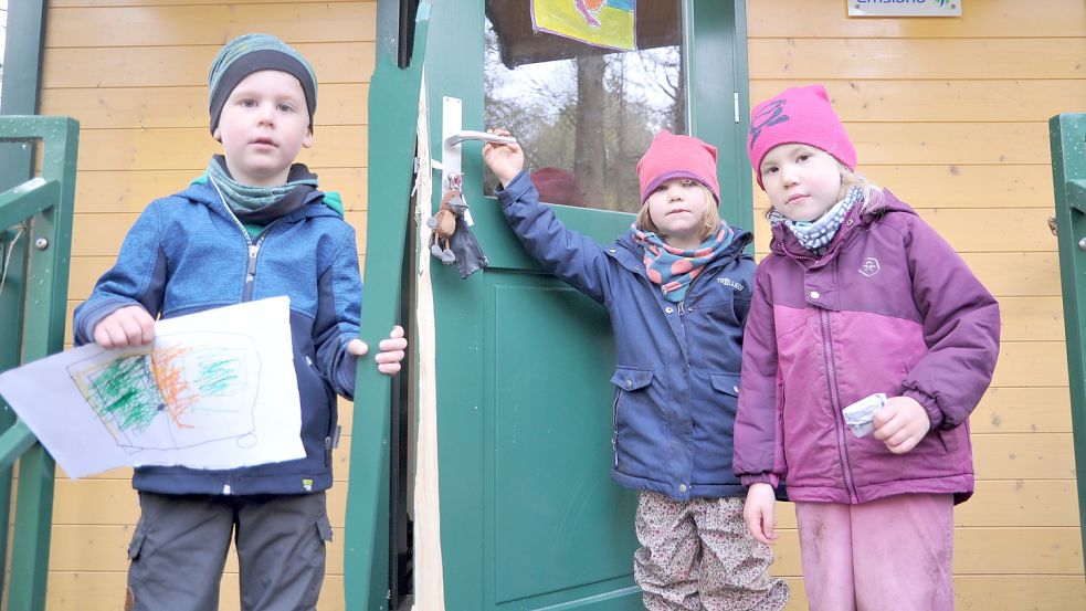 Einbruchsspuren: Die schwer beschädigte Tür des Bauwagens zeigen die vierjährigen Oskar Kösters, Ida Scheffler und Klara Behnen (von links). Oskar hat außerdem ein Bild zu der Tat gemalt. Foto: Schade