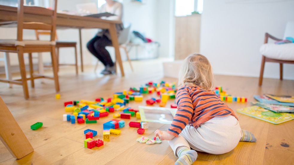 Ein Kind spielt im Wohnzimmer, während seine Mutter im Homeoffice an einem Laptop arbeitet. Foto: dpa/Julian Stratenschulte