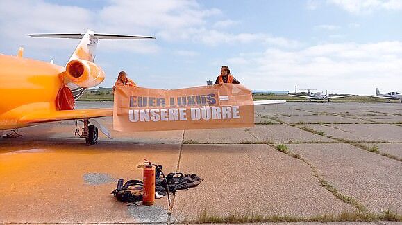 „Euer Luxus = Unsere Dürre“ steht auf dem Plakat, das die Aktivisten der „Letzten Generation“ zusätzlich zu der Farbe an dem Flugzeug auf Sylt angebracht haben. Foto: Letzte Generation