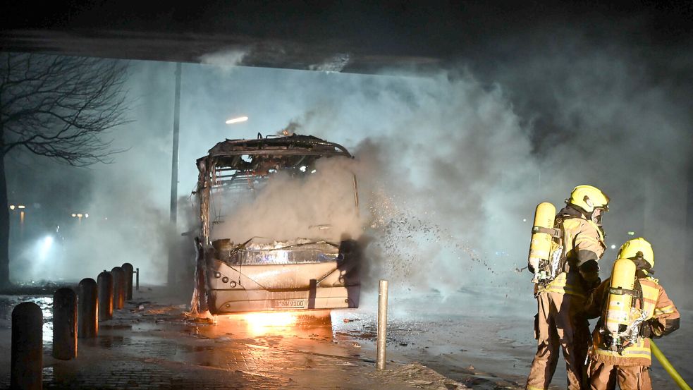 Einsatzkräfte der Feuerwehr löschen in der Silvesternacht in Berlin einen Bus. Foto: dpa/Paul Zinken