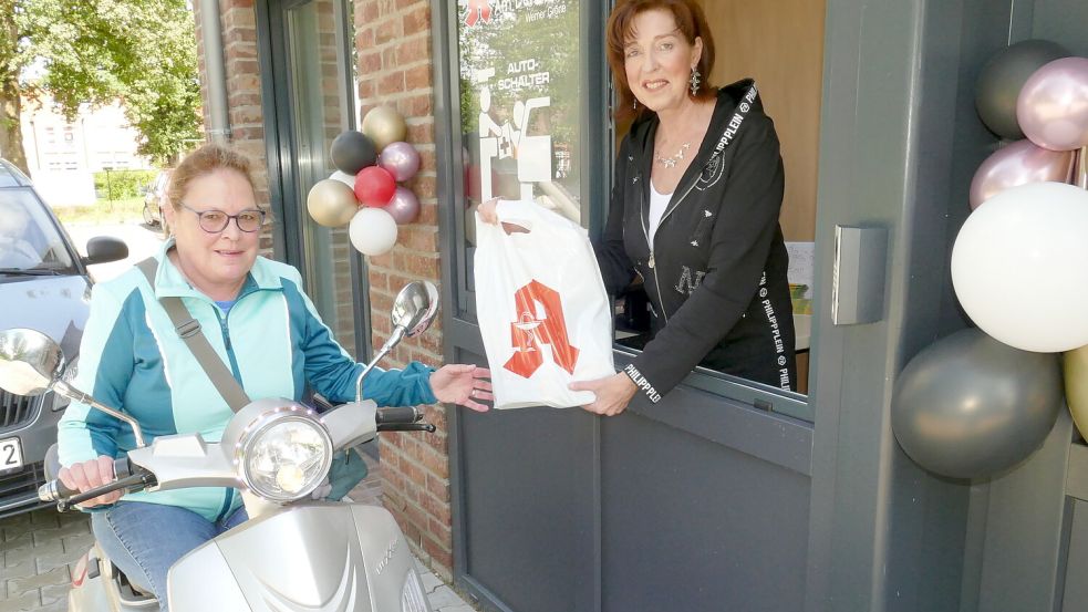 Auch Tina Bron braucht nicht von ihrem Elektro-Trike absteigen, wenn ihr Käthe Müller von der Apotheke am Denkmal in Flachsmeer ihre Bestellungen am Drive-in-Schalter rausreicht. Hinter Tina Bron steht ein Auto. Auch dieser Fahrer muss nur sein Fenster runterkurbeln. Foto: Wieking