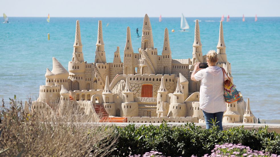 Eine Touristin fotografiert ein filigrane Sandburg in der Nebensaison am Strand von Arenal auf der Insel Mallorca. Foto: dpa/Clara Margais