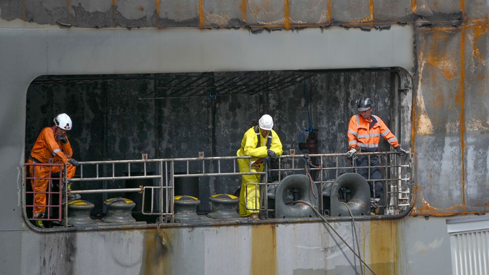 Arbeiter beaufsichtigen an Bord des schwer beschädigten Autofrachters „Fremantle Highway“ das Anlegemanöver im Hafen. Gut eine Woche nach Ausbruch des Feuers war das etwa 200 Meter lange Schiff über Stunden zu dem Nordsee-Hafen an der Emsmündung geschleppt worden. Foto: Penning/DPA