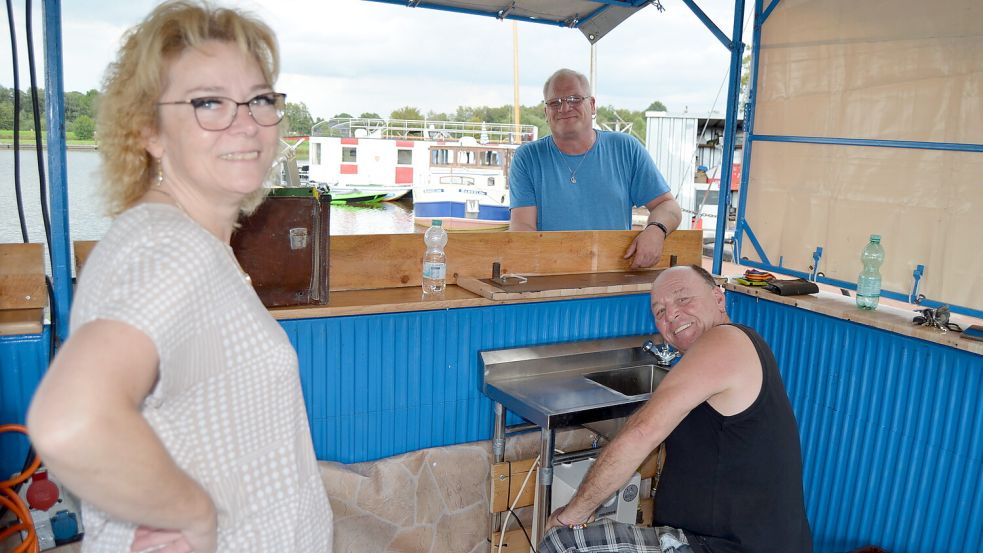 Claudia Otten und Jochen Vagonias sehen Adolf Otten dabei zu, wie der den Warmwasserboiler für den Imbissstand des CB-Funkclubs Sierra Alfa Barßel-Saterland installiert. Der Verein ist seit vielen Jahren beim Hafenfest mit dabei. Er bietet Pommes, Bratwurst und Grillsteaks an. Foto: Fertig