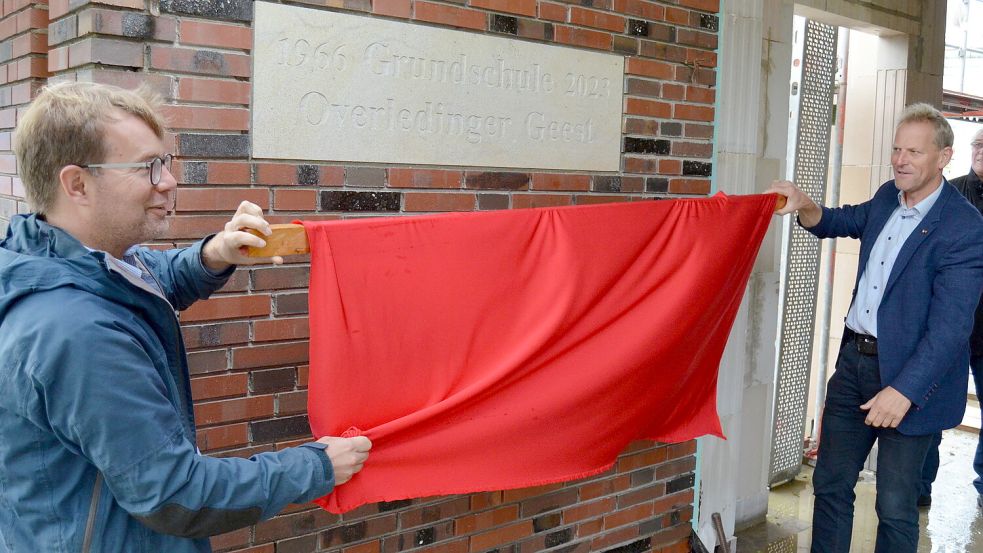Feierlich enthüllten Schulleiter Timo Dogs (links) und Rhauderfehns Bürgermeister Geert Müller die ins Mauerwerk eingelassene Tafel mit den Erbauungsdaten des Schulgebäudes. 1966 entstand es als damalige Mittelpunktschule, nun ist die Jahreszahl 2023 hinzugekommen, weil die Schule nach einem Brand 2021 erneuert und erweitert wird. Foto: Fertig
