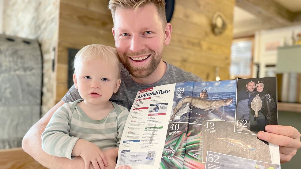 Jan-Philipp Prins zeigt zusammen mit Sohn Hansen eines der Kutter&Küste-Magazine, in denen über den Fehntjer und seine Frau Kira beim Brandungsangeln berichtet wird. Foto: Janßen