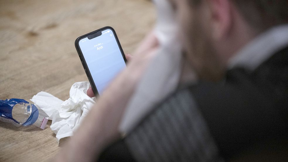 Ein Mann hält ein Taschentuch in einer Hand und ein Telefon mit dem Schriftzug „Arzt“ in der Anderen. Foto: Albert/DPA