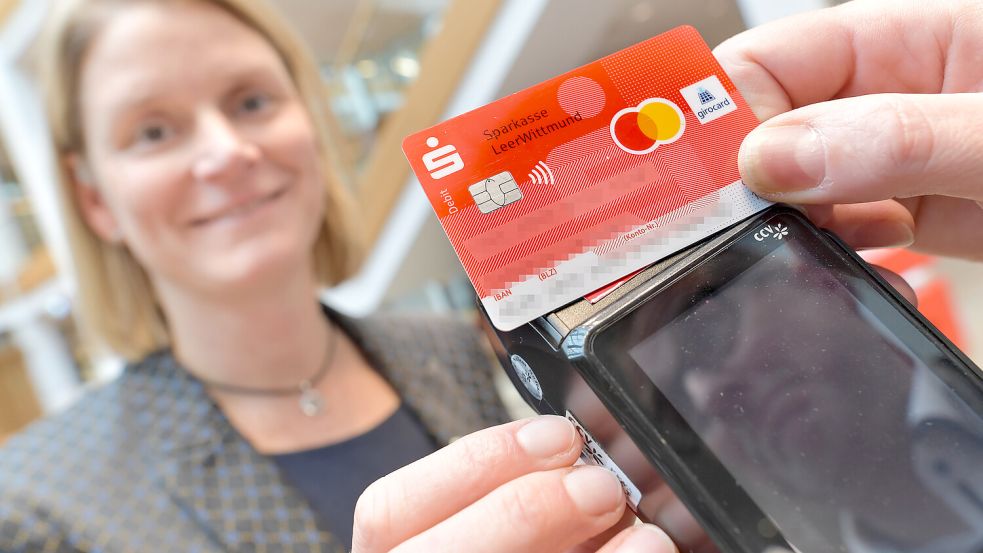 Inga Coordes von der Sparkasse Leer-Wittmund hält ein Kartenlesegerät, auf dem eine neue Sparkassen-Karte mit einer Debitkarten-Funktion von Mastercard gelegt wird. Foto: Ortgies