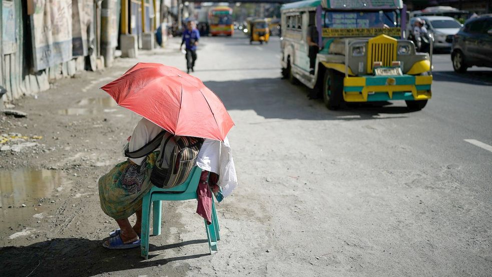 Eine Straßenverkäuferin schützt sich in Manila mit einem Regenschirm vor der Sonne. Foto: Aaron Favila/AP/dpa