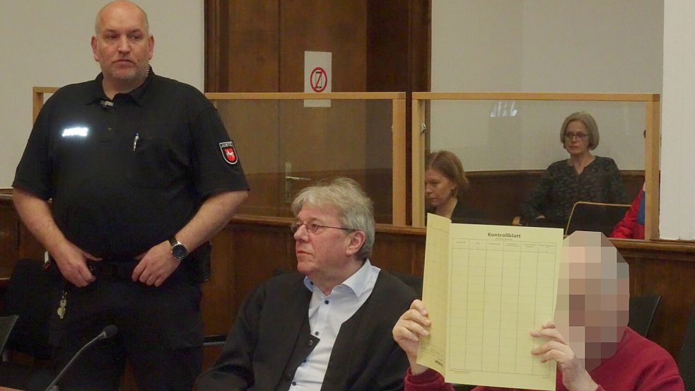 Der Angeklagte sitzt im Gerichtssaal neben seinem Verteidiger Michael Schmidt und hält sich einen Aktendeckel vors Gesicht. Foto: Luppen