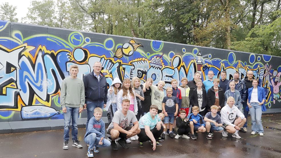 Die jungen Künstlerinnen und Künstler vor der fertig gestalteten Wand des Barßeler Tennisvereins mit den Sponsoren, den Verantwortlichen vom Barßeler Jugend- und Begegnungszentrum sowie den Vereinsvorsitzenden vom Tennisverein und Barßeler Ruderverein. Dessen Vereinsheim wird als nächstes verschönert. Foto: Passmann