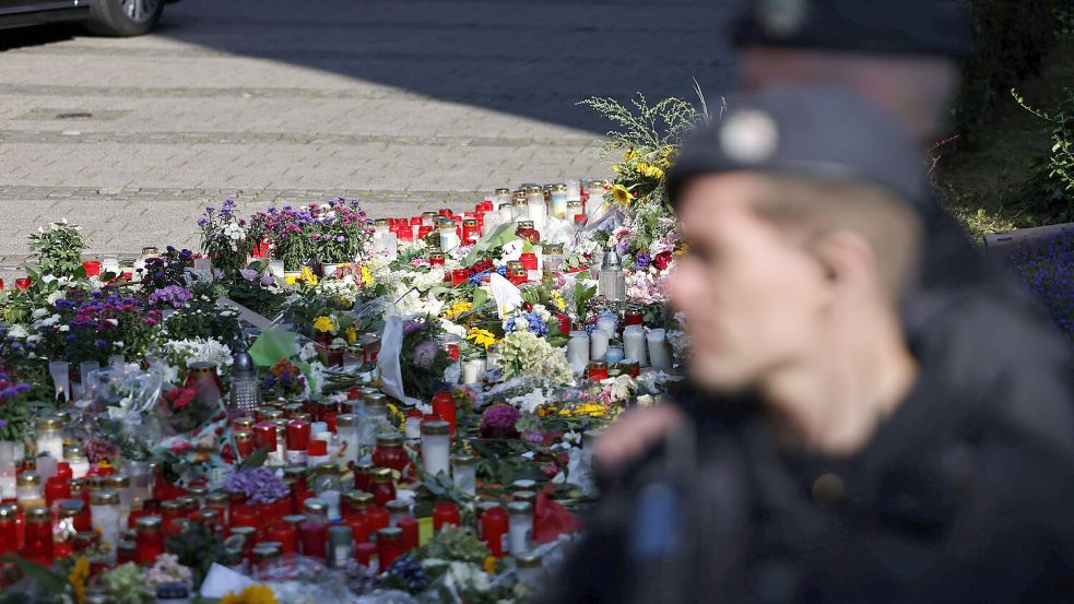 Ein Polizist steht vor Blumen, die Menschen in der Nähe des Tatorts abgelegt haben, um der drei Todesopfer zu gedenken. Foto: IMAGO / Panama Pictures