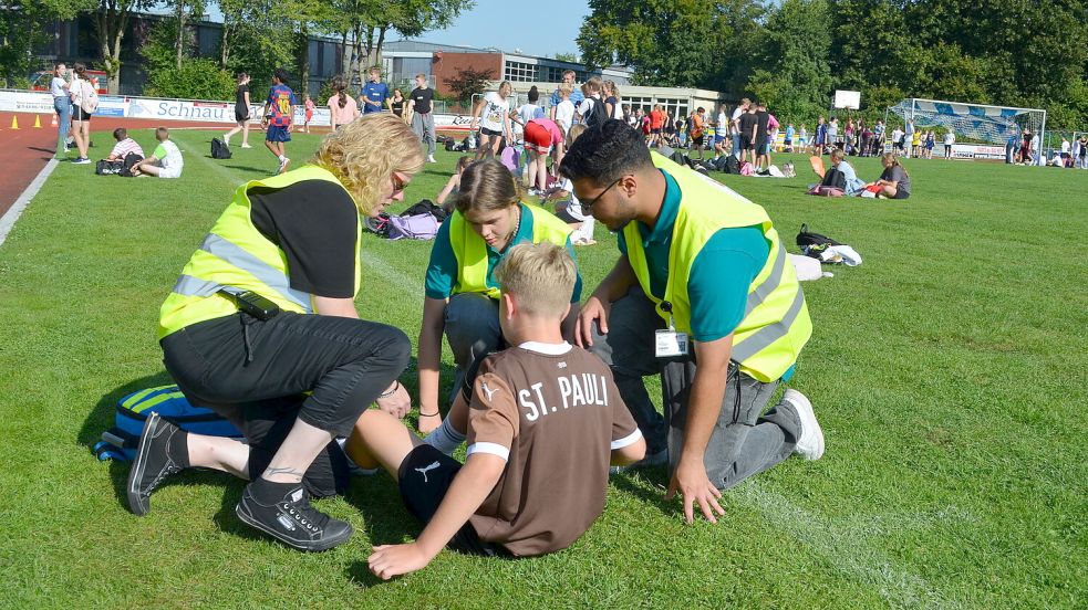 Erste Hilfe bei einem Siebtklässler, der nach einem Lauf Knieprobleme hatte, leisten hier bei den Bundesjugendspielen am Schulzentrum Saterland (von links) Lehrkraft Eva Schulte und die beiden Schulsanitäter Sarah Fischer und Hamza Dabbagh. Foto: Fertig