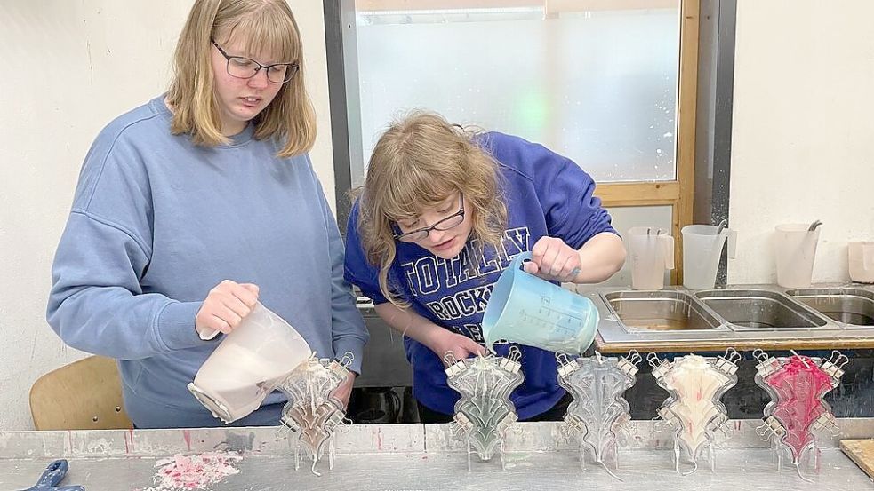 Kurz vor Ostern gießen Bianca Marx (links) und Nathalie Peters flüssiges Wachs in die auf den Kopf gestellten Formen. Die so produzierten Kerzen in Weihnachtsbaumform werden in der Vorweihnachtszeit im Altenoyther Werkstattladen und in vielen anderen Geschäften verkauft. Foto: Stix