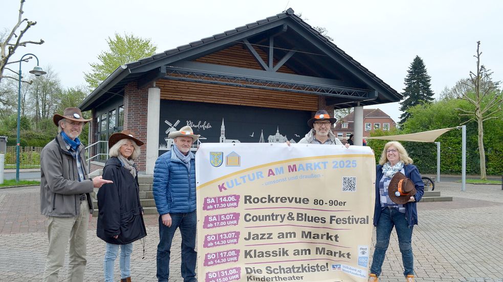 Ein Teil des Ehrenamtler-Teams der KAM vor der Marktbühne in Rhauderfehn mit einer der sechs Plakatwände, auf denen das Sommerprogramm 2025 bekanntgemacht wird (von links): Norbert Knitsch, Eva Gorny-Ulma, Theodor Voß, Manfred Schmäing und Almuth Strenge. Foto: Astrid Fertig