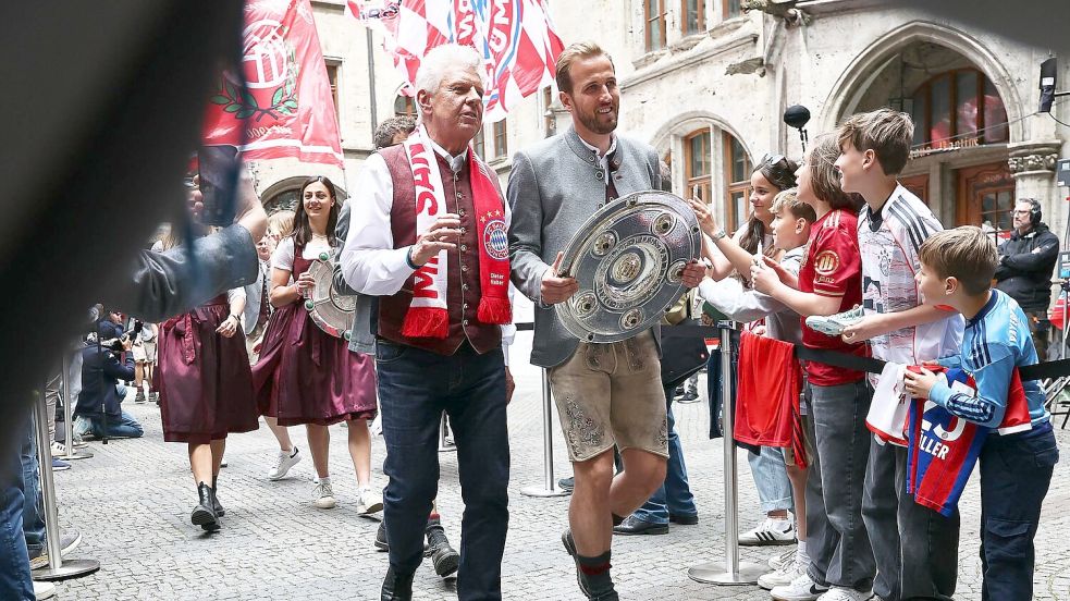 Bundesliga-Torschützenkönig Harry Kane trägt die Meisterschale flankiert von Oberbürgermeister Dieter Reiter (mit Fanschal) ins Münchner Rathaus. Foto: Daniel Löb/dpa
