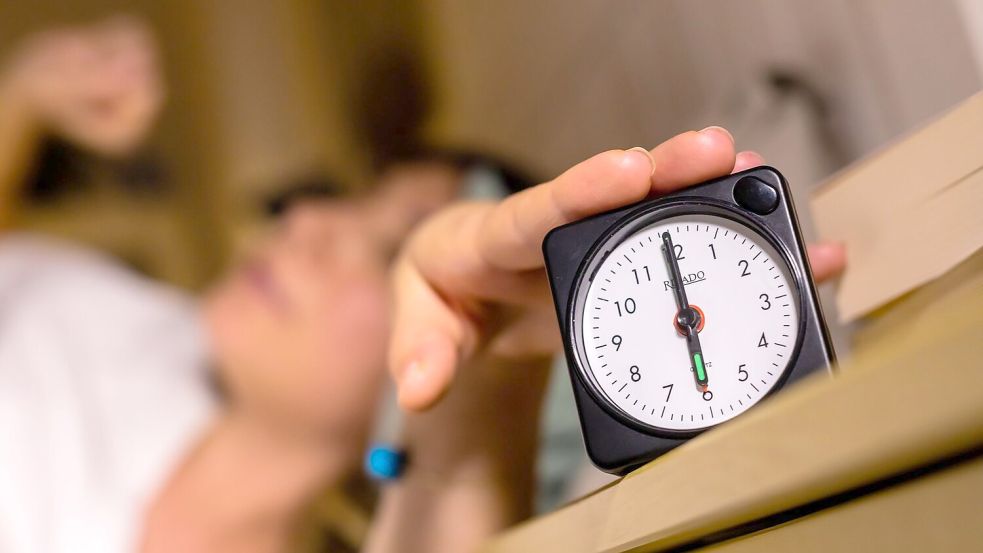 Eine Frau schaltet vom Bett aus einen auf sechs Uhr gestellten Wecker aus. Foto: Christoph Soeder/dpa