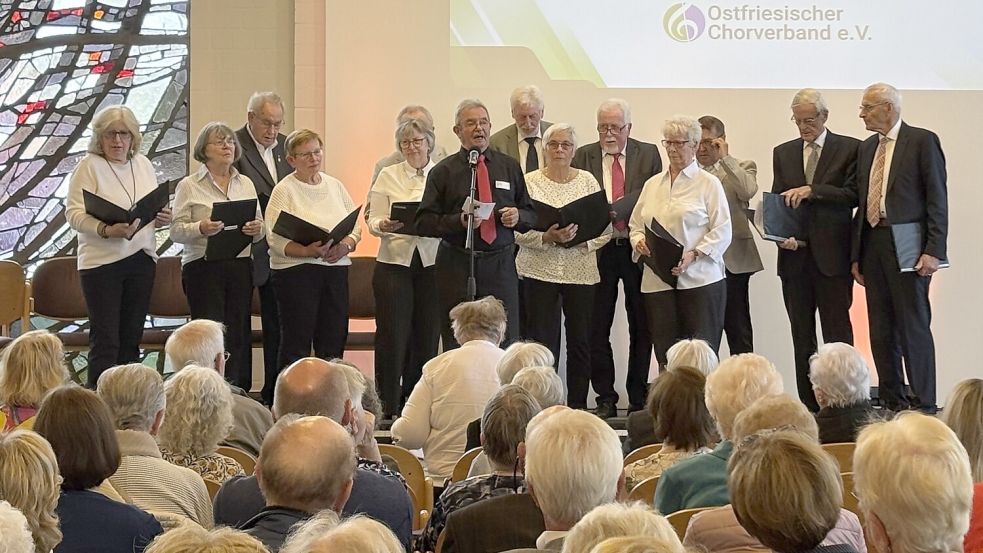 Der Vizepräsident des Ostfriesischen Chorverbandes, Diethelm Sempell (Mitte, am Mikrofon) aus Ihrhove, begrüßte die 260 Gäste. Anschließend trat die Chorgemeinschaft Rhauderfehn (MGV Immergrün Westrhauderfehn/Gemischter Chor Feierabend Rhaudermor) auf. Foto: Marius Ammermann