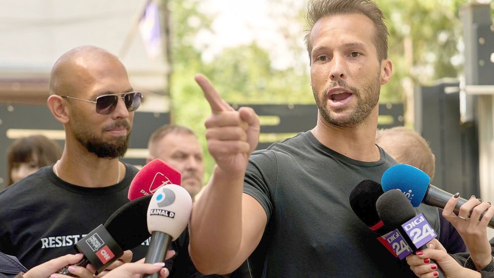 Andrew Tate (links) schaut zu seinem Bruder Tristan Tate, der am 21. Mai vor einer Polizeistation in Voluntari in Rumänien redete. Foto: Vadim Ghirda/AP/dpa
