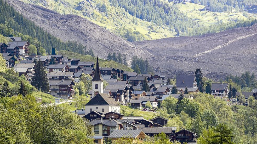 Das Dorf Kippel wurde verschont, dahinter ist die Wüste aus Eis, Schlamm und Fels zu sehen. Foto: Jean-Christophe Bott/KEYSTONE/dpa