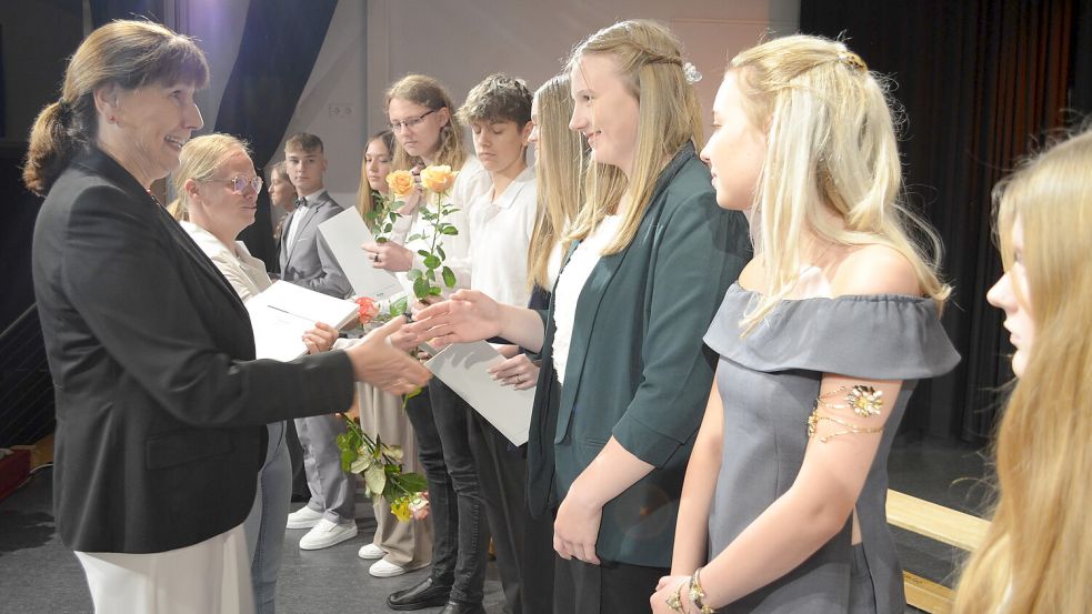 Hier überreicht Astrid Fedorowicz, Schulleiterin der Haupt- und Realschule Saterland, Jule Gerdes von der Klasse 10R1 ihr Abschlusszeugnis. Wiebke Krause, die Vorsitzende des Schulfördervereins überreicht jedem der Abschlussschüler dazu eine Rose. Foto: Astrid Fertig