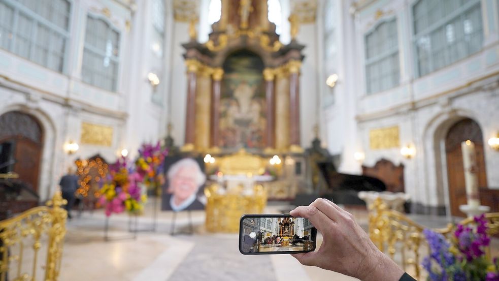 Ein Besucher macht zu Beginn der Trauerfeier ein Foto mit einem Smartphone. Foto: Marcus Brandt/dpa