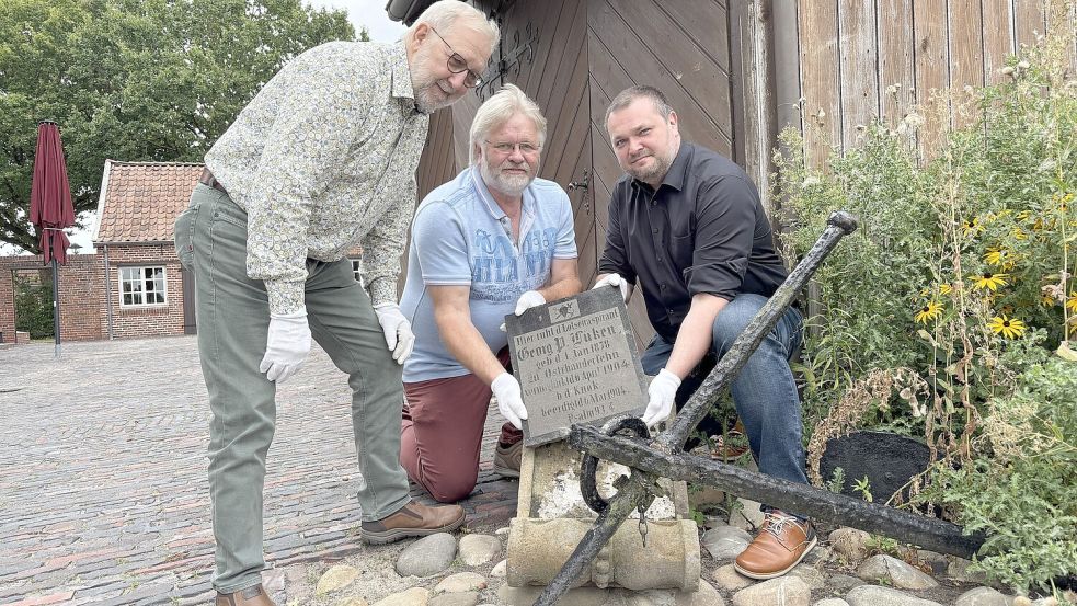 Hermann Drieling (von links), Hinrich Heselmeyer und Marcus Neumann zeigen den Grabstein von Georg P. Lüken aus Ostrhauderfehn. Foto: Dirk Hellmers