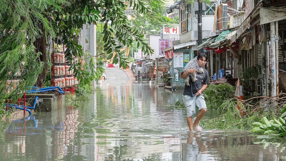 Ein Anwohner trägt in Hongkong ein Haustier durch das Hochwasser. Foto: Chan Long Hei/AP/dpa