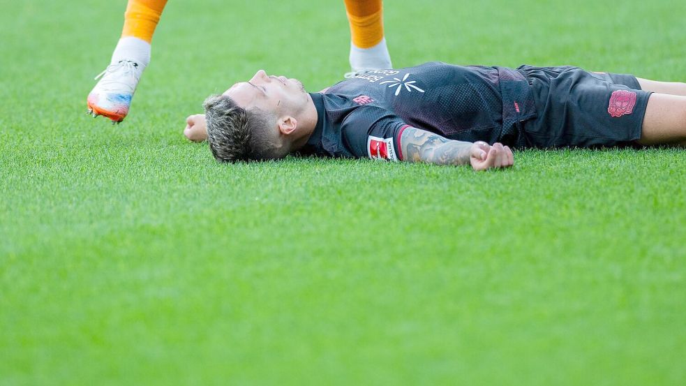 Bayer Leverkusens Kapitän Alejandro Grimaldo liegt nach einem Zusammenprall mit dem eigenen Mann benommen auf dem Boden. Foto: Rolf Vennenbernd