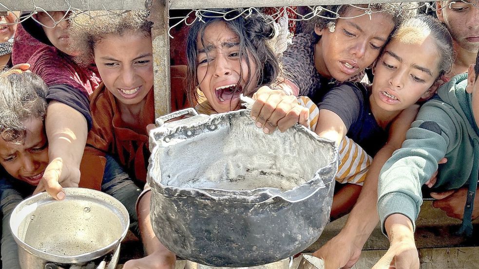 Kinder versuchen in Chan Junis im Gazastreifen mit ihren Töpfen Nahrungsmittel zu bekommen, die von Wohltätigkeitsorganisationen verteilt werden. Foto: Moaz Abu Taha/APA Images via ZUMA Press Wire/dpa