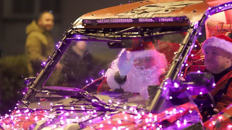 Ein als Weihnachtsmann verkleideter Mann winkt aus einem beleuchteten Fahrzeug während einer Traktor-Lichterfahrt. Foto: Sascha Thelen/dpa