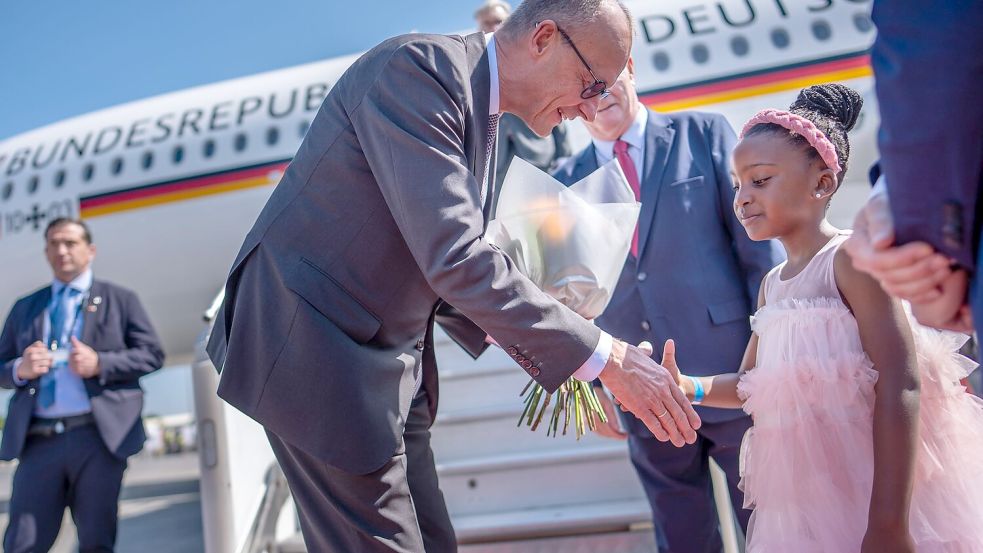 Kanzler Friedrich Merz wird auf dem Flughafen von Johannesburg von einem Mädchen begrüßt. Foto: Michael Kappeler/dpa