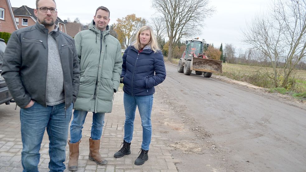 Maik Stegemerten, Frank Renken und Daniela Preyk wohnen an der Siedlungsstraße in Klostermoor zwischen Weihnachtsmannweg und Gronewoldstraße. Wegen der Flurbereinigung war die Strecke monatelang eine Schlammpiste. Nun liegt die Baustelle bis zum Frühjahr 2026 still. Das ist für die Anwohnerinnen und Anwohner unbefriedigend. Foto: Astrid Fertig