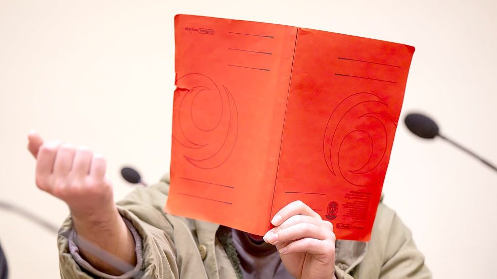 Der Angeklagte verdeckte sein Gesicht zum Prozessauftakt zunächst mit einer Mappe. Foto: Peter Kneffel/dpa