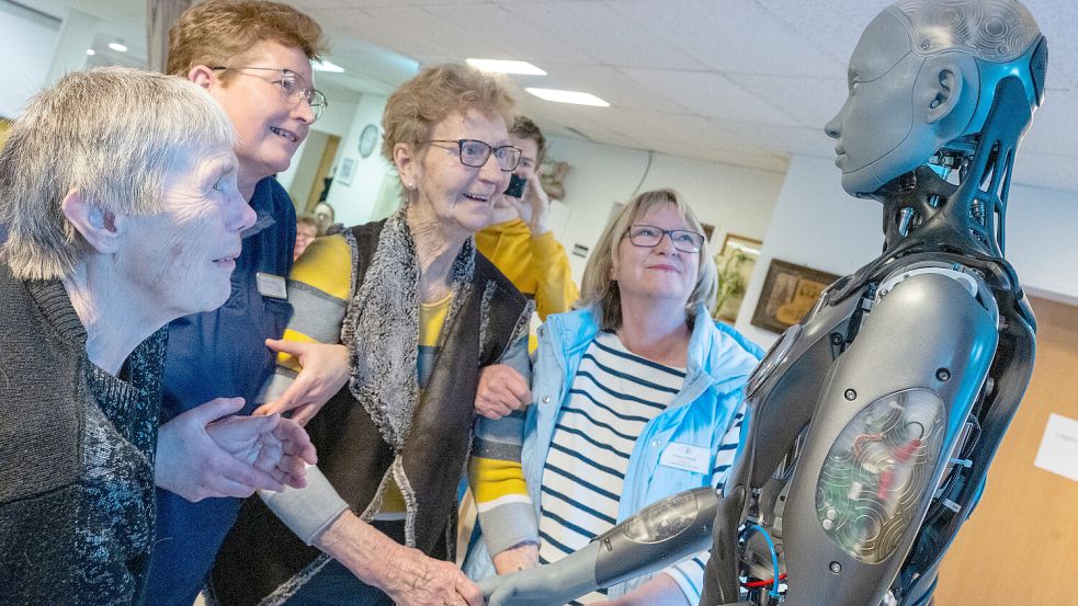 Ein Roboter zum Anfassen – und was er für weiche Hände hat! Bewohnerin Johanna Kück (von links), Betreuerin Claudia Lindner, Bewohnerin Marga Ehlert und Irene Preyk, Leiterin für soziale Betreuung hatten im Haus Friede ihren Spaß mit Ameca. Im Hintergrund schießt FSJ-ler Okko Schier ein Erinnerungsfoto. Foto: Klaus Ortgies