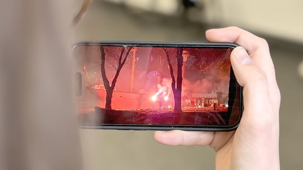 Eine Person steht mit Leuchtfackeln (vielleicht Bengalos) beim Feuerschiff am Emder Delft. Das Foto wurde bei Facebook kurz nach Mitternacht in der Nacht zu Dienstag, 24. März 2026, hochgeladen. Foto: Mona Hanssen