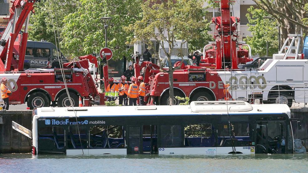 Der Linienbus wird von Kränen aus dem Fluss geborgen. Foto: Thomas Samson/AFP/dpa