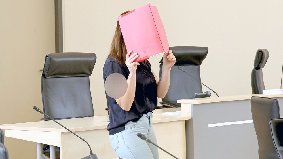Die Angeklagte betritt den Gerichtssaal mit rotem Aktendeckel vor dem Gesicht. Foto: A7120 Bernd Wüstneck