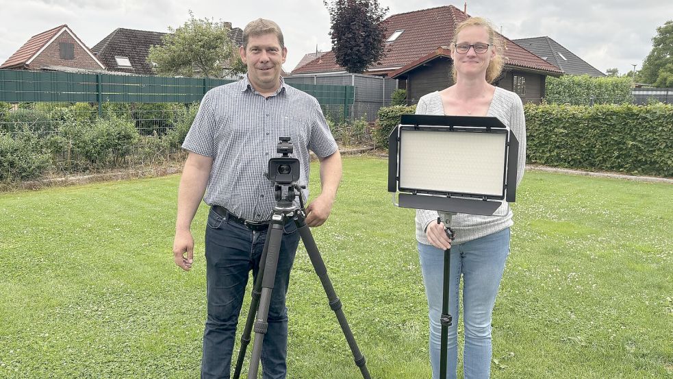 Michael (links) und Stephanie Schmidt in ihrem Garten: Michael steht hinter der Kamera auf dem Stativ, Stephanie hinter der Videoleuchte auf dem Stativ – mit dieser Ausrüstung wollen die beiden für das Projekt „Zeit.Zeugen Saterland“ die Erinnerungen von Zeitzeugen als kurze Videos festhalten. Foto: Horst Kruse