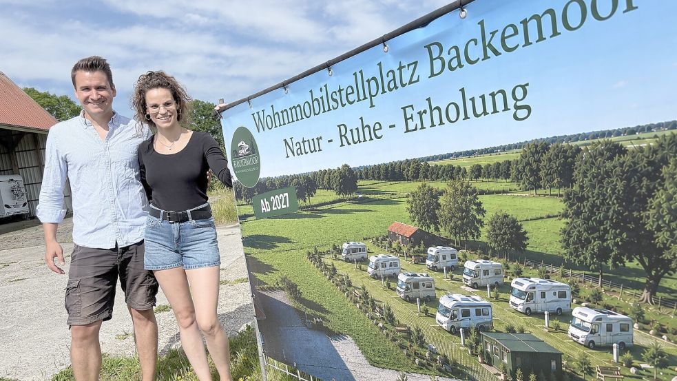 Am Standort des geplanten Wohnmobilstellplatzes in Backemoor weisen Hilke und Johannes Baumann mit einem Banner auf den erhofften Start in 2027 hin. Foto: Marion Janßen