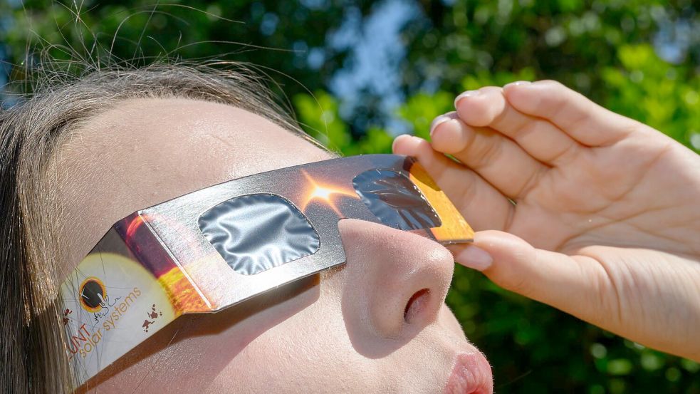 Eine junge Frau schaut durch eine Sonnenfinsternisbrille und betrachtet die Mittagssonne. Foto: Patrick Pleul